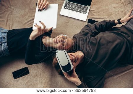 Attractive Young Couple Using Devices Together, Tablet, Laptop, Smartphone, Headphones Wireless. Com