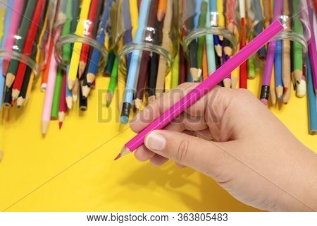 A Pink Pencil Is In The Hand Of A European Girl. Close-up Photo On A Bright Yellow Background. A Lot
