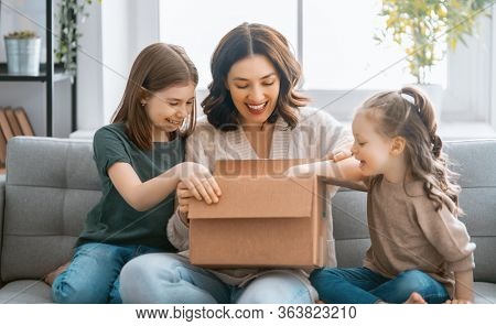 Mother and daughters are unpacking cardboard box at home.