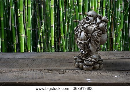 Budai On A Wooden Table With Bamboos In The Background