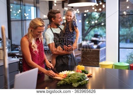 Caucasian family enjoying their time at home together, standing in a kitchen, using a laptop, a woman is cutting vegetables, social distancing and self isolation in quarantine lockdown during