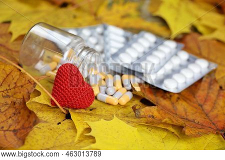 Knitted Red Heart And Pills On Autumn Maple Leaves, Selective Focus. Hypertension, Heart Disease And