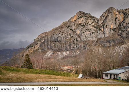 Surba Town Hiding Behind Trees At The Foothill Of Pyrenees Mountains. Rocky, Bare Mountain Peaks, Ta
