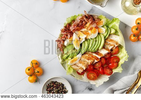 Cobb Salad With Grilled Chicken, Eggs, Avocado, Tomato, Bacon On Marble White Background. Classic Am