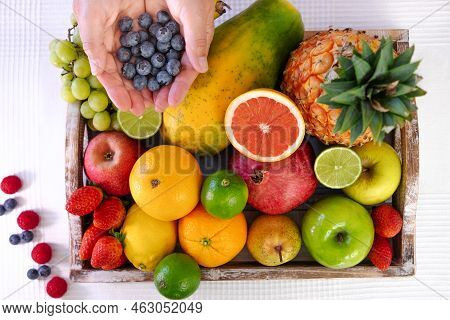 Above View Of Wooden Basket Full Of Fresh Colorful Fruits. Mature Woman's Hands Holding Group Of Blu