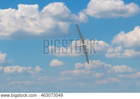 A Light Glider Plane Flies In The Blue Sky With White Clouds.