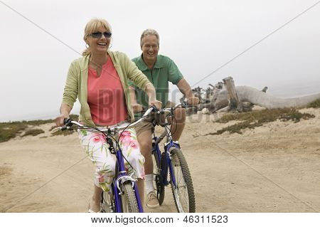 Cheerful middle aged couple riding bicycles along the beach