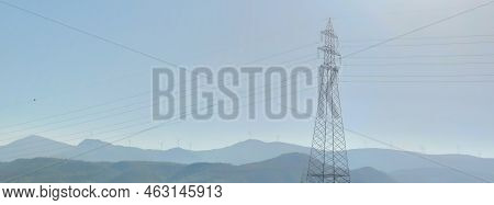 High Voltage Post Or High Voltage Tower On Background Mountains With Wind Turbines