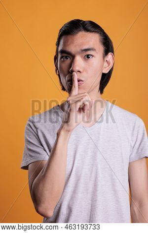 Young Asian Man Showing Silence Gesture, Making Tsss Sign. Serious Teenager Loking At Camera With Fo