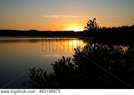 Sunset With Reflection On A Swedish Lake In Smalland With Bushes In The Foreground On The Shore. Rom