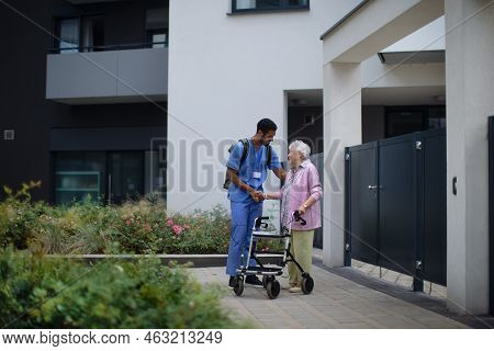 Caregiver Walking With Senior Woman Client In Front Of Nurishing Home.