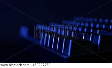Black Mechanical Gaming Computer Keyboard Illuminated In The Dark By Blue Light From A Monitor Scree