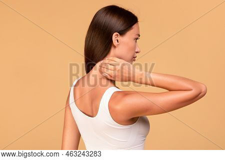 Young Woman Touching And Self Massaging Her Neck, Rubbing Skin, Standing Over Beige Studio Backgroun