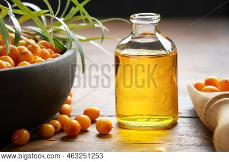 Bottle Of Sea Buckthorn Essential Oil, Bowl Of Sandthorn Berries, Wooden Scoop Of Sea Buckthorn Berr
