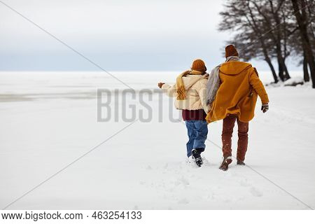 Back View At Carefree Young Couple Running Outdoor In Winter By Frozen Lake, Copy Space