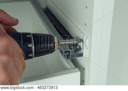 Male Hands Hold Cordless Electric Screwdriver, Screw To Fix Rail, Assembling Drawer Of White Dresser