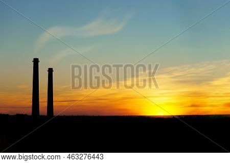 Two Industrial Pipes With Smoke Against The Sunset Sky.