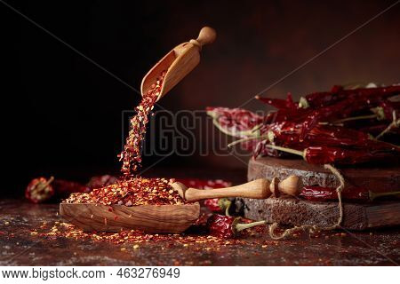 Chilli Flakes Are Poured Into A Wooden Dish. Chilli Flakes And Dried Chili Peppers On A Brown Backgr