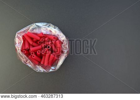 Red Tubetti Rigati Pasta In A Bag On A Gray Background. Beet Pasta In The Form Of Small Tubes.