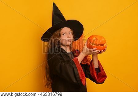 Cute Halloween Child Girl In Wizard Costume With Carved Pumpkin Or Jack O Lantern Pumpkin Looking At