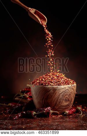 Chilli Flakes Are Poured Into A Wooden Dish. Chilli Flakes And Dried Chili Peppers On A Brown Backgr