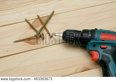 Table With Tool. Electric Screwdriver On A Wooden Table. Side View Of The Black Metallic Screws, Ele
