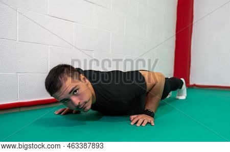 Determined Strong Young Man Doing Push-ups And Looking At Camera. He Is Dressed In An Orange Shirt A
