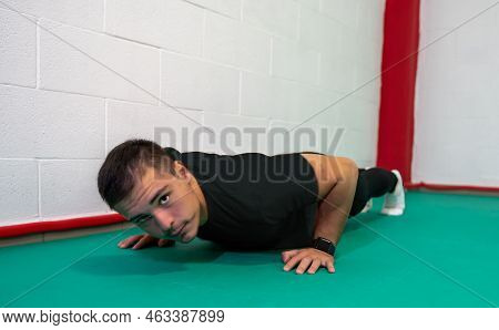 Determined Strong Young Man Doing Push-ups And Looking At Camera. He Is Dressed In An Orange Shirt A