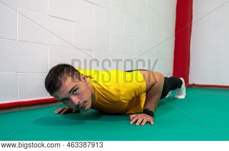 Determined Strong Young Man Doing Push-ups And Looking At Camera. He Is Dressed In An Orange Shirt A