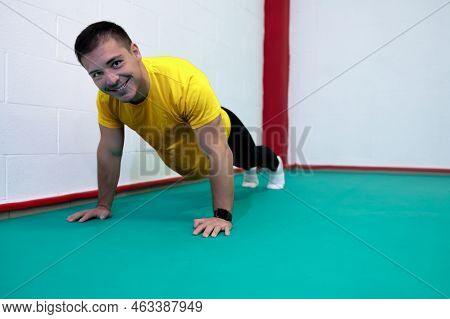 Portrait Of A Strong Determined Young Man Doing Push-ups And Looking At Camera Smiling. He Is Dresse