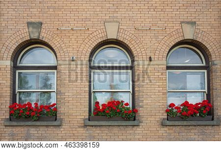 Three Vintage Windows With Stone Frames And Flowers On Shelf. Three Arch Windows Old House With Red 