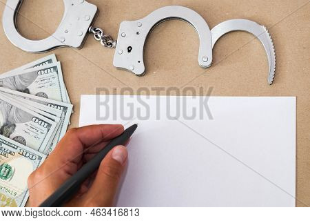 A Hand In Handcuffs Sits At A Table In Front Of A Blank Sheet Of Paper And A Pen. Concept: The Detai