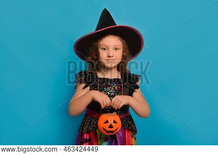 Cute Little Girl In Halloween Witch Dress Or Wizard Costume Holding Pumpkin Candy Basket Or Jack O L