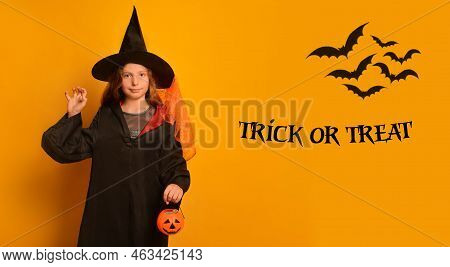 Little Witch Girl In Wizard Student Costume Showing Boo Gesture Holding Halloween Pumpkin Candy Bask