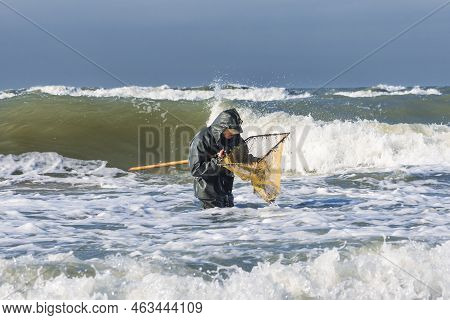 Amber Catching In The Baltic Sea. Amber Catcher Or Fisherman With Fisherman\\\'s Coat And Boots Into