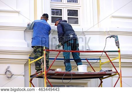 Workers Repair The Building Wall Standing On Lifting Platform. Two Builders Painting The House Facad