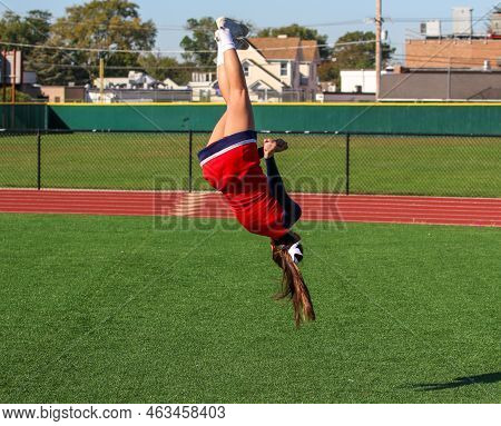 A High School Cheerleader Is Flipping And Twisting Updide Down In The Air While Warming Up For Pep R