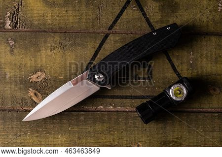 Pocket Knife And Flashlight On An Army Crate. Knife And Lantern On The Table. A Sharp Knife And A Sm
