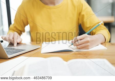Young Asian Female Student Studying Online Using Laptop And Holding Mobile Phone Surfing The Interne