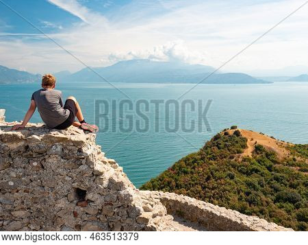 Tired Blond Hair Boy It On The Stony Wall Of Ruin Rocca Di Manerba, Garda Lake, Italy.