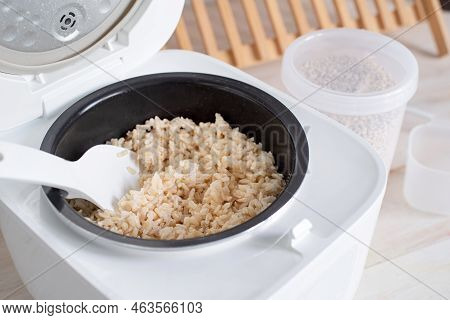 Opened Electric Rice Cooker With Cooked Steaming Brown Rice On Wooden Counter-top In The Kitchen