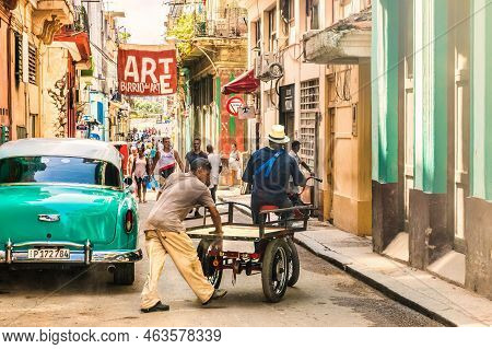 Havana, Cuba - July 18 2018 : Carts And Vintage Cars With An Art Sign Above The Street