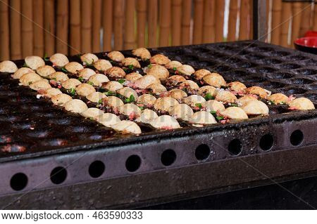Japanese Street Food Takoyaki At Special Grill Pan. Process Of Cooking Takoyaki Balls With Octopus F