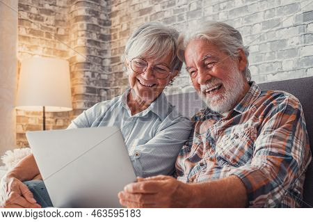 Cute Couple Of Old People Sitting On The Sofa Using Laptop Together Shopping And Surfing The Net. Tw