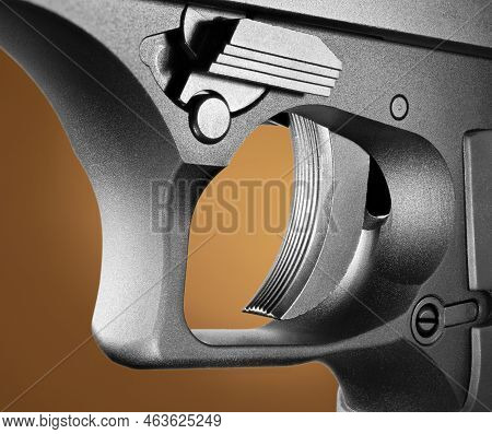Closeup Of A Large Semi-automatic Handgun\'s Trigger That Is Textured For Grip On An Orange And Brow