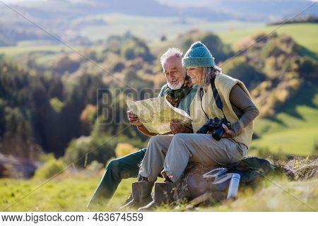 Senior Couple Having Break, Looking Into Paper Map During Hiking In Autumn Nature.