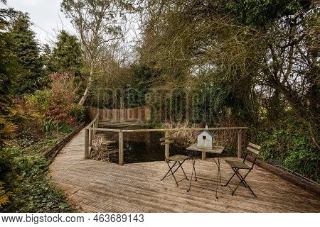 Stradishall, England - March 21 2016: Private Garden Deck Area With Table And Chairs, Fenced Pond, M