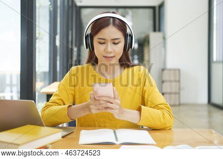 Young Asian Female Student Studying Online Using Laptop And Holding Mobile Phone Surfing The Interne