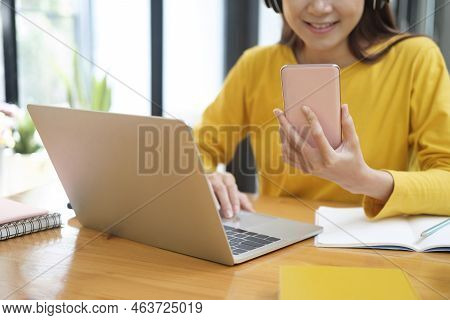Young Asian Female Student Studying Online Using Laptop And Holding Mobile Phone Surfing The Interne