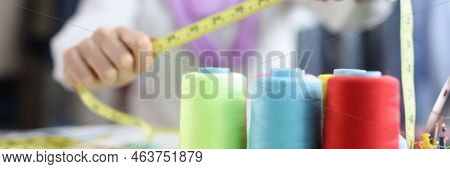 There Are Bobbins With Threads On The Seamstresss Table, Close-up, Blurry. Woman In Atelier Showing 